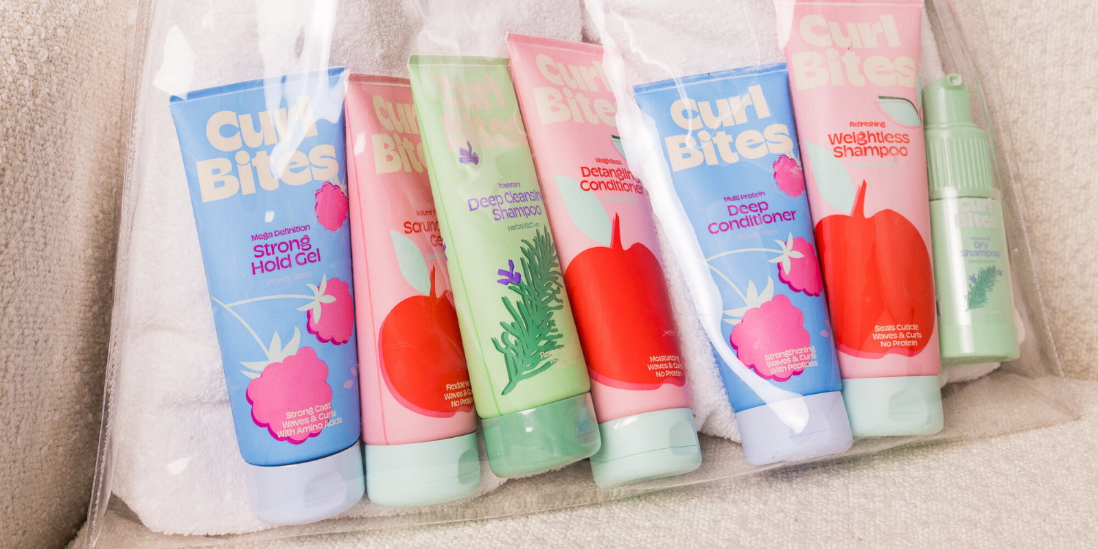 Mehrere Curl Bites Haarpflegeprodukte, darunter Shampoos, Conditioner und Styling-Gel, liegen nebeneinander in einer transparenten Tasche.