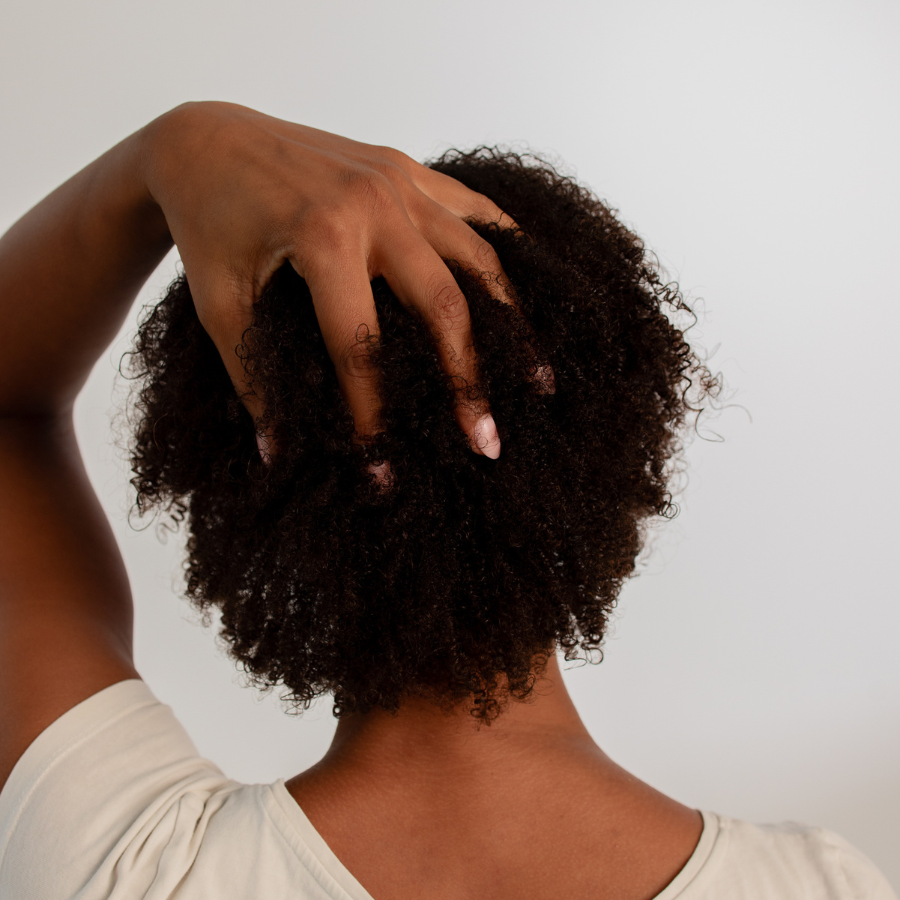 Person mit sehr dichtem, kurzem Afro-Haar von hinten, eine Hand greift ins Haar am Hinterkopf.