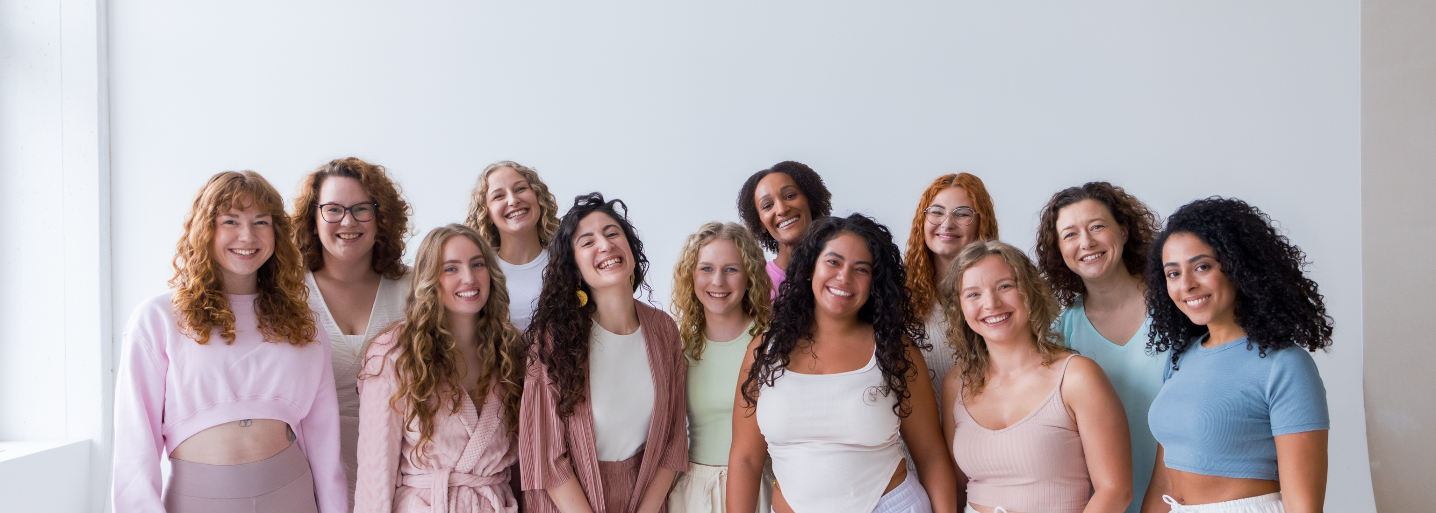 Gruppenfoto von zwölf lächelnden Personen mit texturierten Haaren in lockerer Kleidung vor hellem Hintergrund.