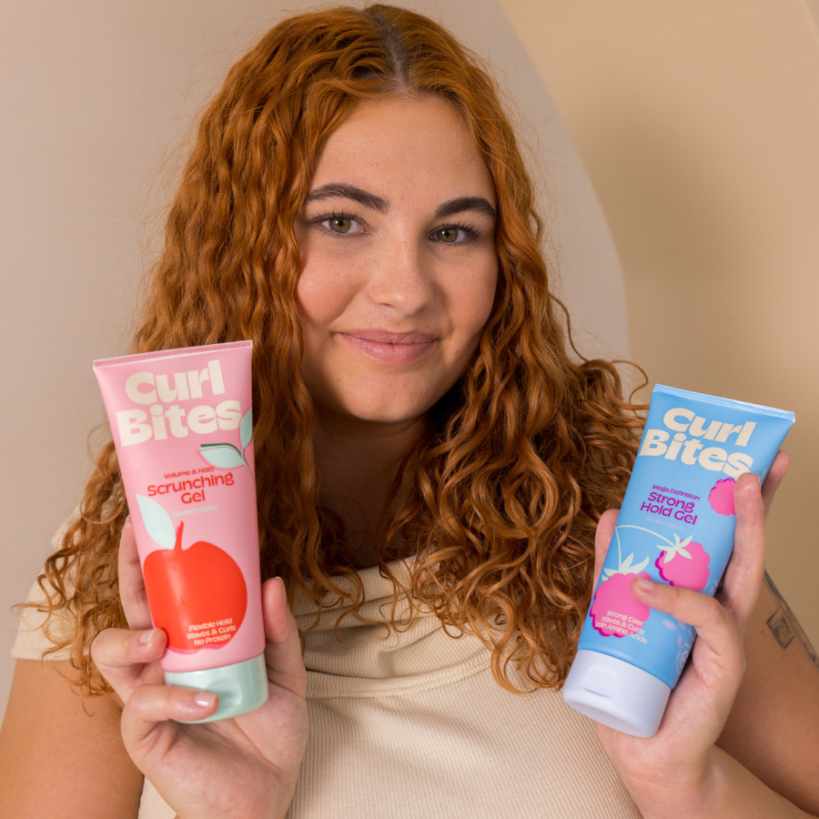 Frau mit lockigem Haar hält zwei Curl Bites Gele in den Händen: das pinke Curl Bites Scrunching Gel und das blaues Strong Hold Gel.