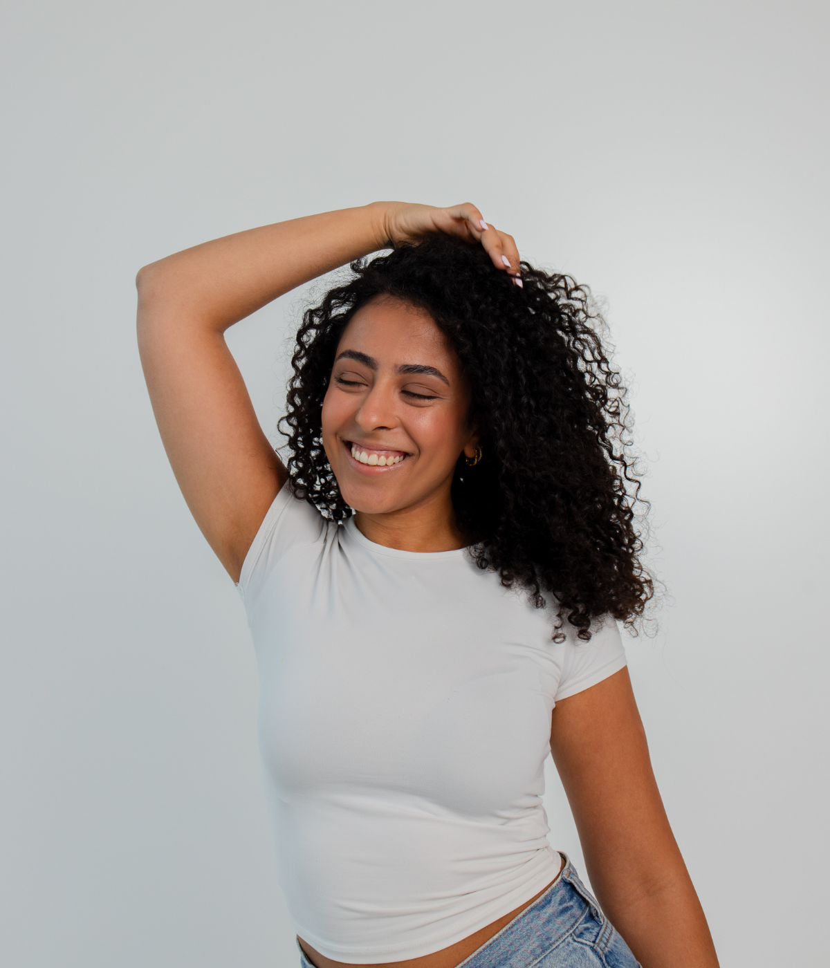 Lächelnde Person mit lockigem Haar berührt den Kopf – führt zu Produktempfehlungen für lockiges Haar.