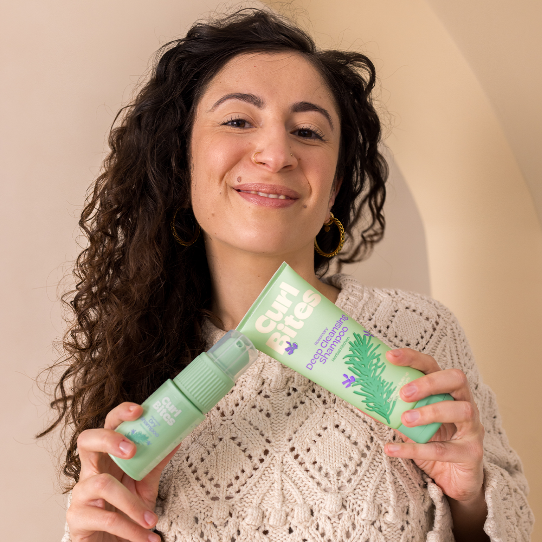 Person mit lockigem Haar hält zwei Shampoo Produkte in der Hand – führt zur Kollektion zur Pflege der Kopfhaut.