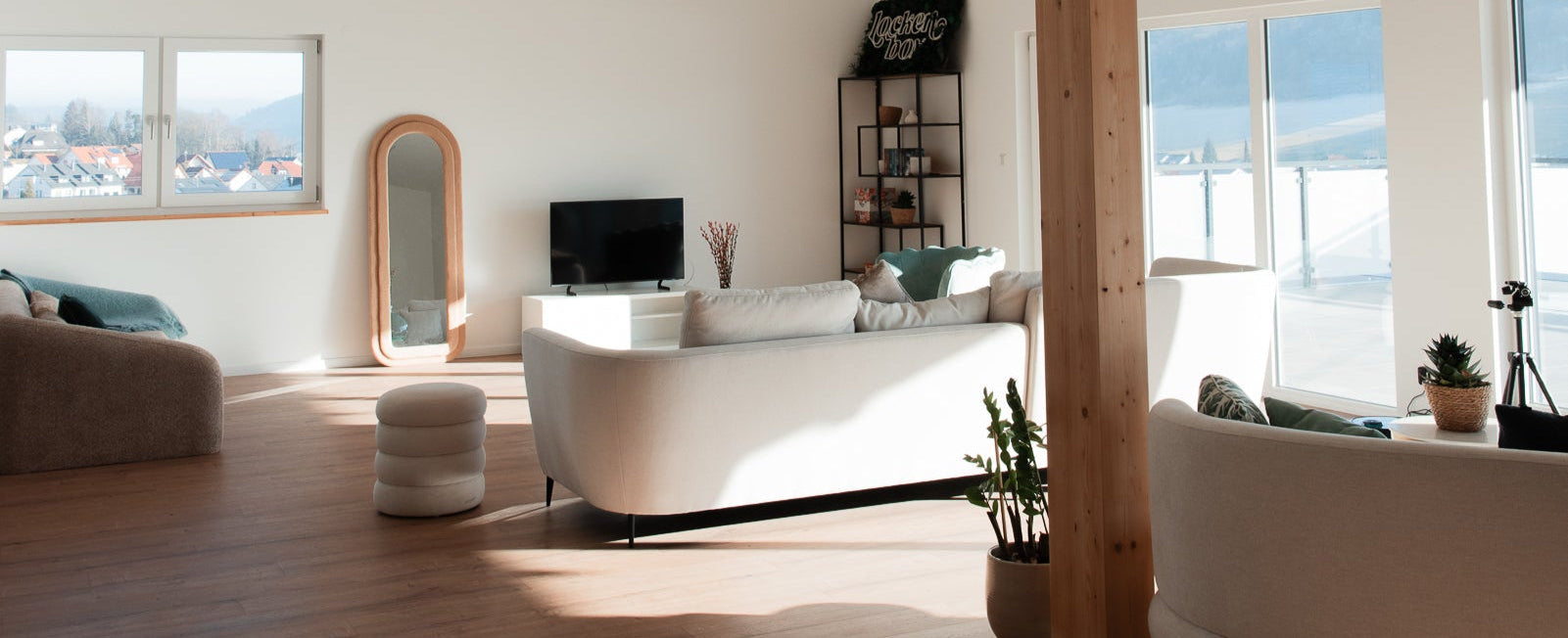 Wohnzimmer des Curl Bites Lofts mit großen Fenstern, hellen Möbeln, Holzfußboden und Blick ins Grüne