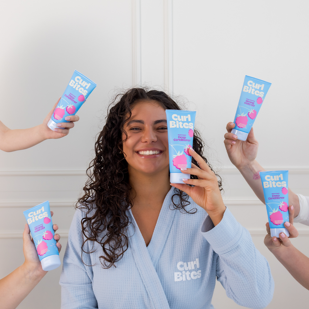 Das Bild zeigt eine Person mit lockigem Haar, die ein Produkt aus der Power Bites Linie (blauer Behälter) in der Hand hält. Weitere Hände präsentieren ebenfalls Produkte dieser Linie.