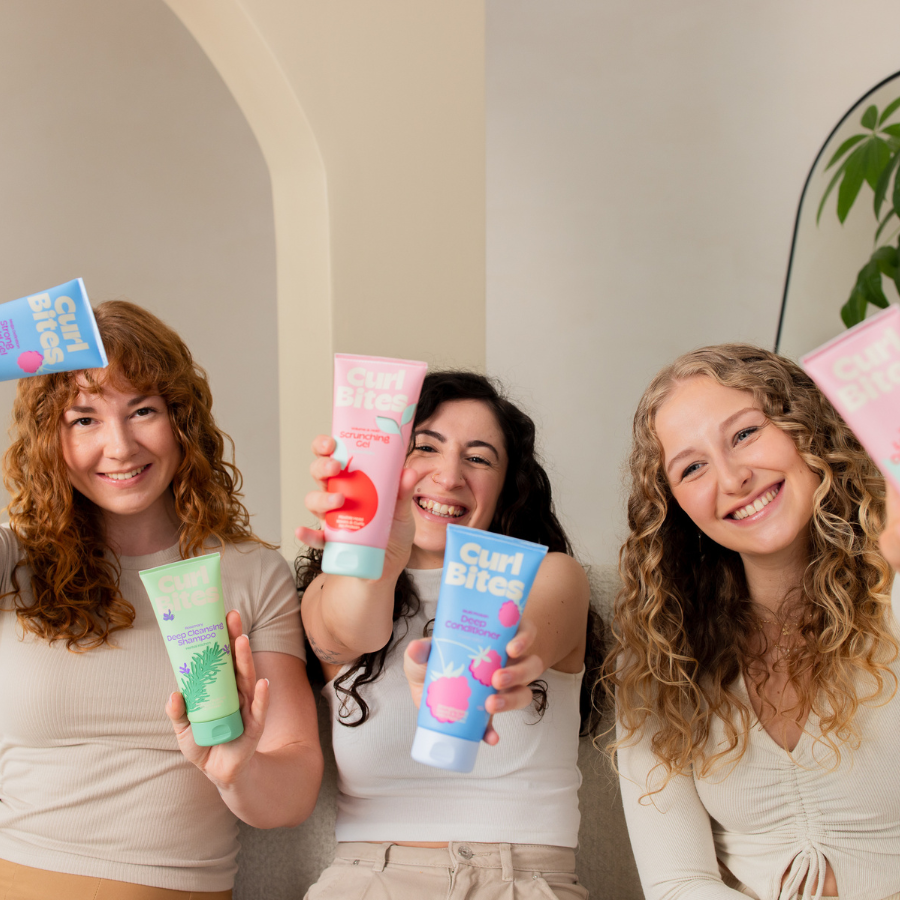 Drei lachende Frauen mit lockigem Haar halten Curl Bites Produkte in die Kamera - führt zu Curl Bites Starter Set